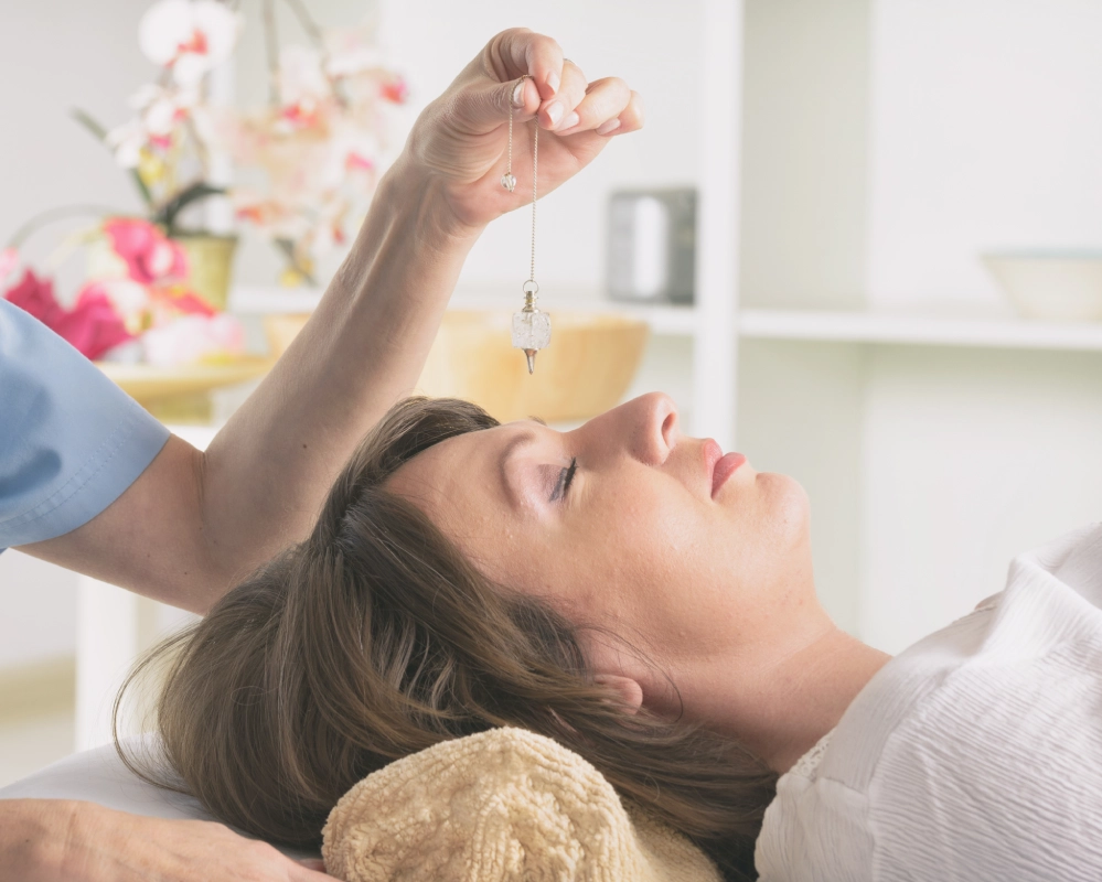 A person offers hypnosis services by holding a pendulum over a woman lying down with closed eyes, suggesting a relaxation or therapy session.