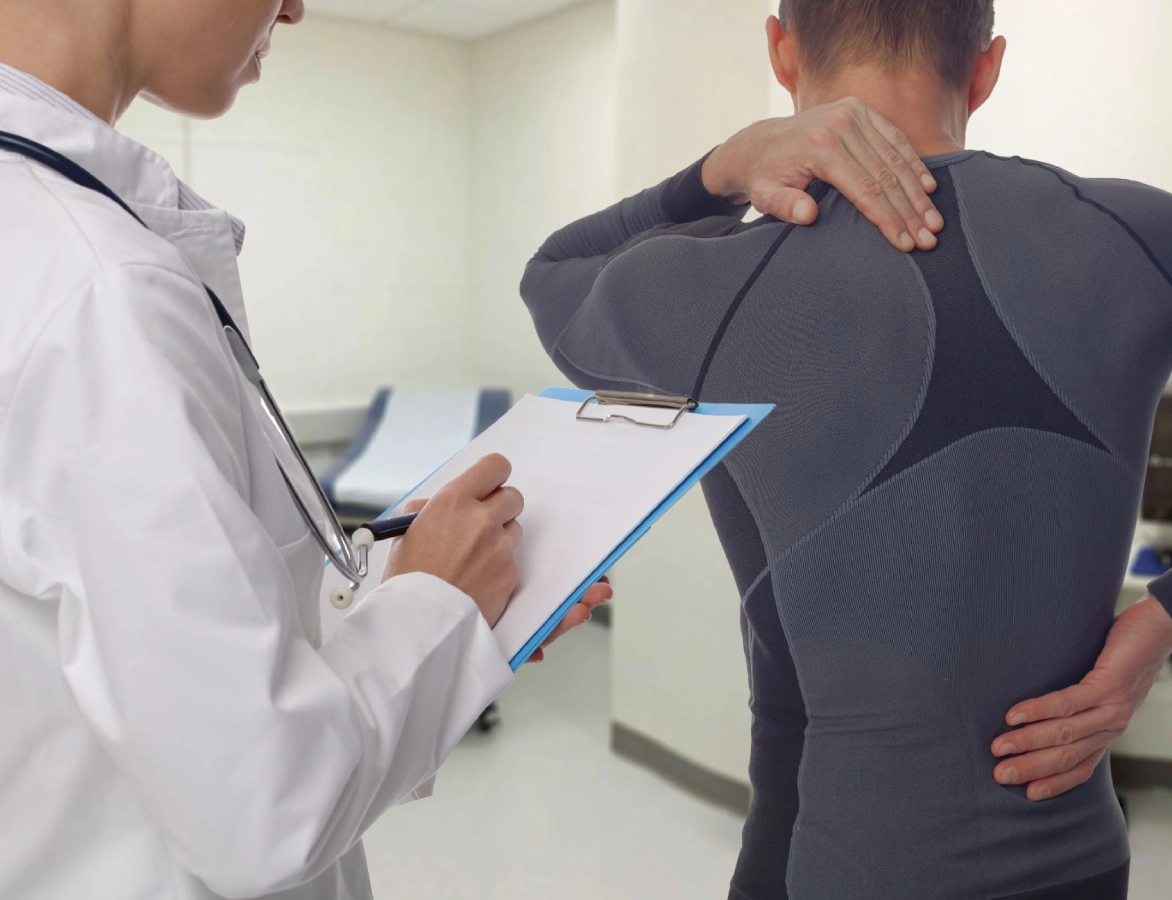 A doctor writes on a clipboard while observing a person using EFT for personal growth as they hold their shoulder in a medical examination room.