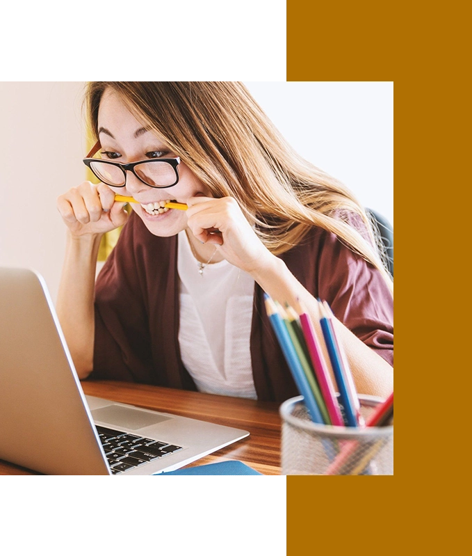 A person with glasses, perhaps an EFT practitioner, bites a pencil in frustration while staring at a laptop. A container brimming with colorful pencils sits in the foreground, offering a splash of inspiration amidst the tension.