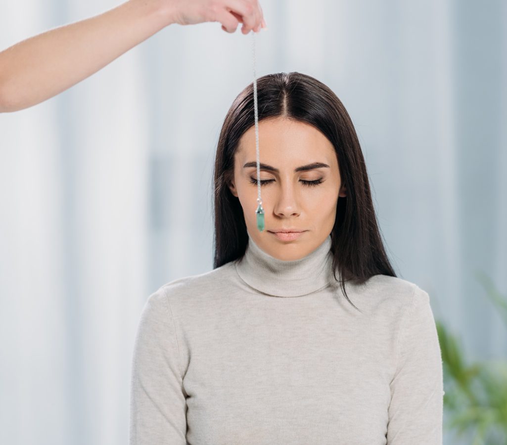 A seasoned EFT practitioner gently swings a pendulum above the head of a person with closed eyes, guiding them into a peaceful state.