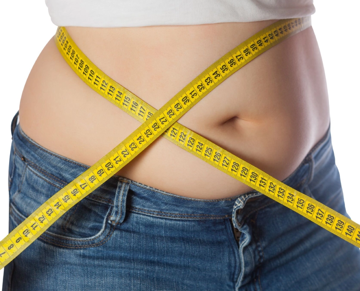 A close-up of a person wearing jeans with a yellow measuring tape wrapped around their waist, reflecting their progress in hypnosis for weight loss.