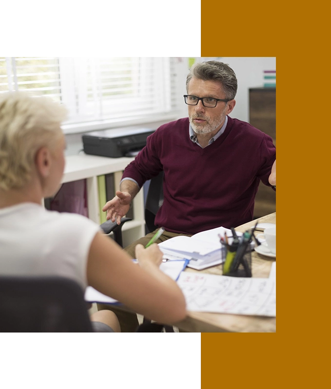 Two people are having a discussion in an office setting, with papers and stationery on the table. Amidst their conversation, they take a moment to practice EFT tapping for stress relief, finding calm and focus amidst their busy day.