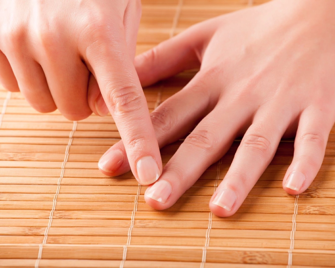 Two hands rest on a bamboo mat, one gently pointing to the nail of the other hand’s finger, as if guiding a journey towards emotional wellbeing through thoughtful therapy and attention.