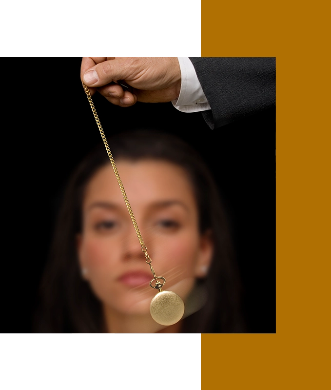 A hand holds a gold pocket watch on a chain, swinging gently in front of a blurred woman, as if guiding her towards emotional wellbeing.