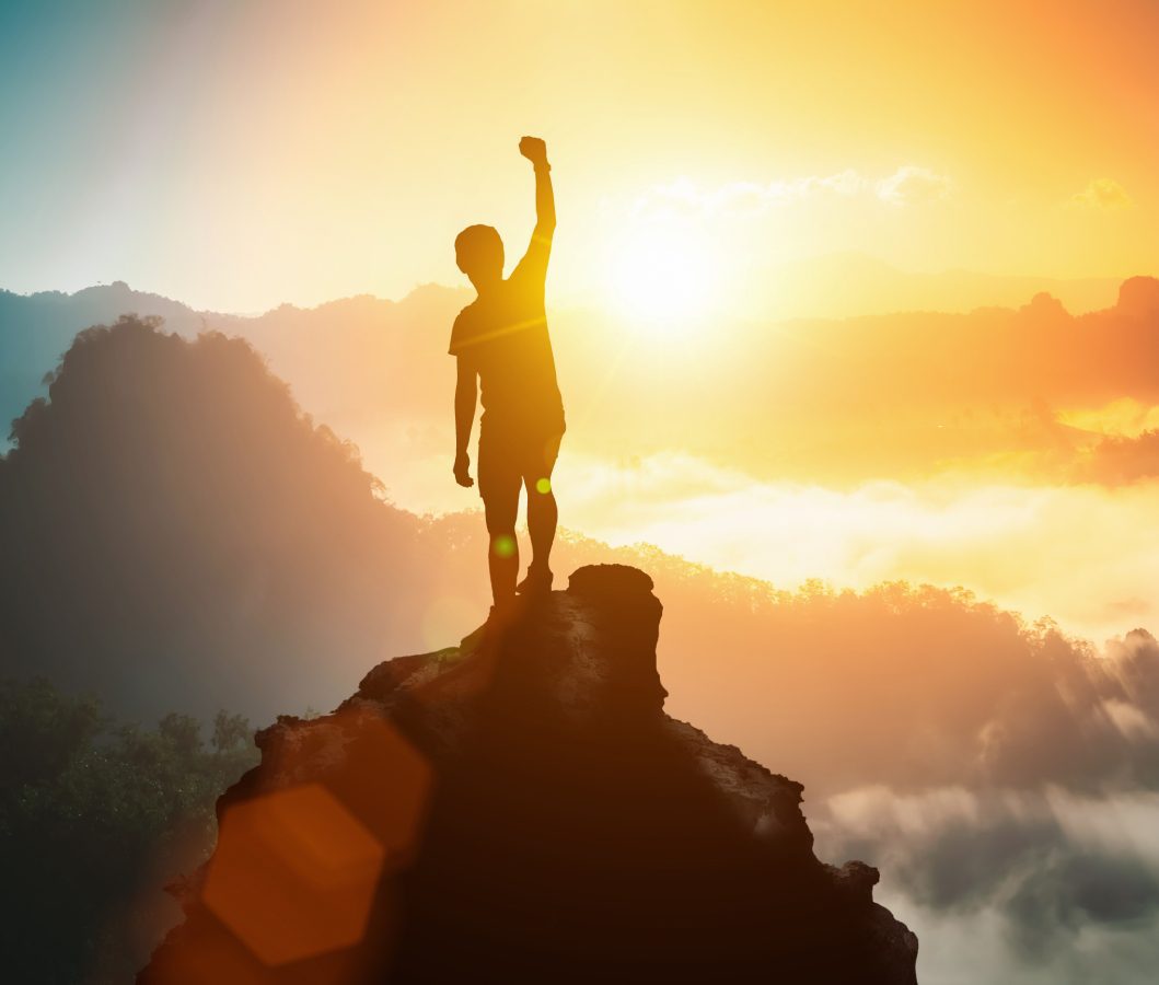 A silhouetted person, having employed hypnosis for personal growth, stands triumphantly on a mountain peak at sunrise.