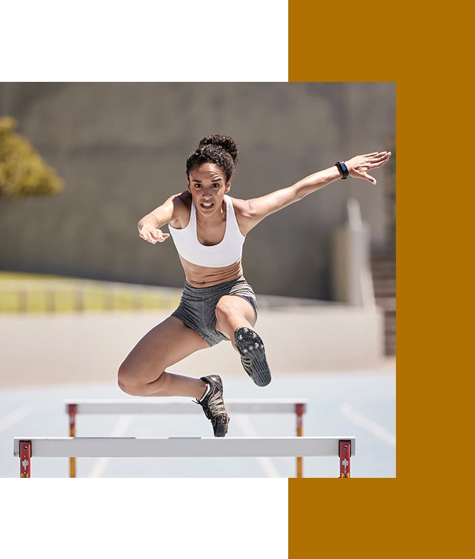 Wearing a sports bra and shorts, the athlete gracefully leaps over a hurdle on the track, embodying the spirit of EFT for Personal Growth, as each stride reflects her journey toward self-improvement and resilience.