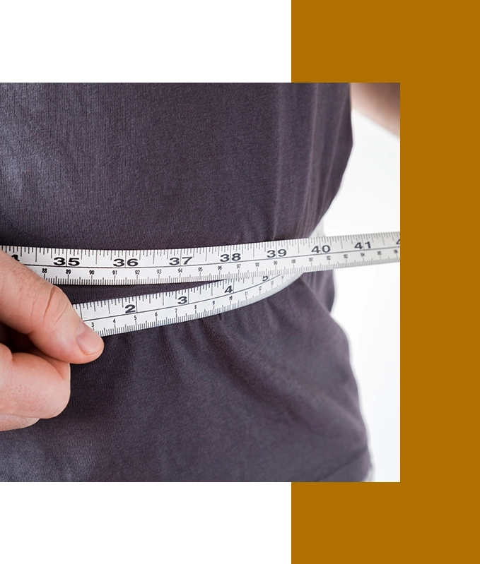 A person measuring their waist with a tape measure, clad in a dark shirt, stands against a backdrop of black and brown borders, contemplating the benefits of hypnosis for weight loss.