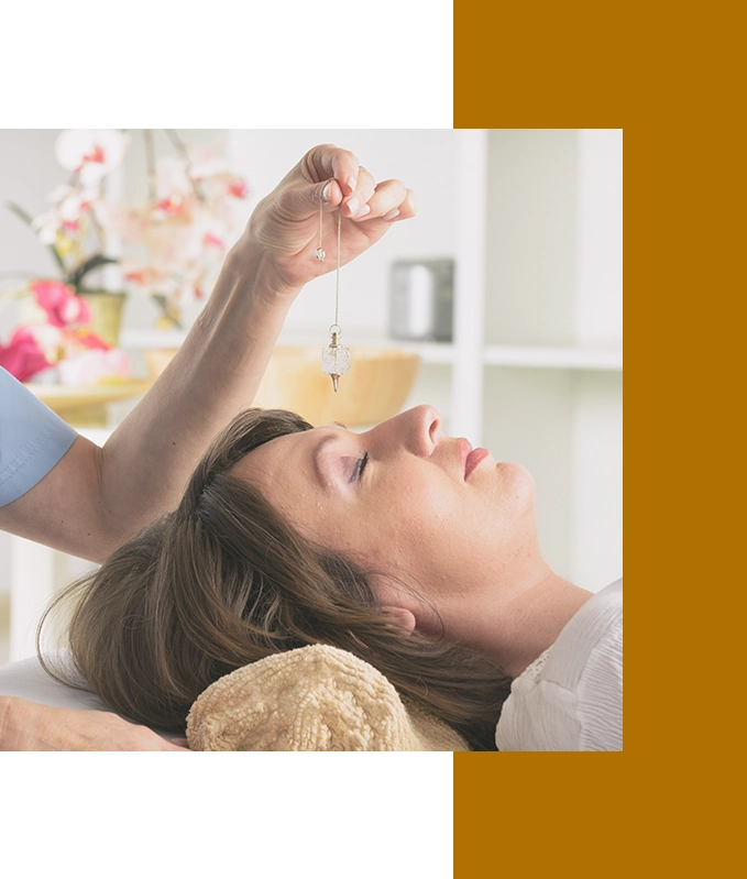 In a bright room filled with flowers, a person lies peacefully while another holds a pendulum above them, practicing hypnosis for anxiety relief.