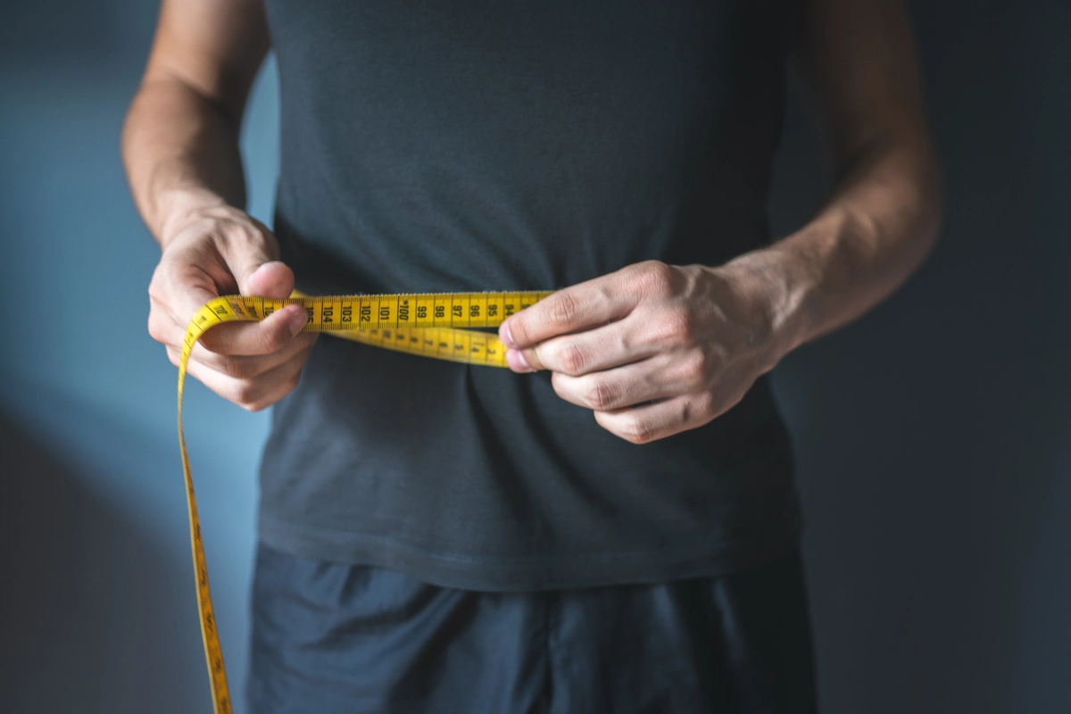 A person in a dark shirt holds a yellow measuring tape in both hands, reminiscent of the precision seen in hypnosis for weight loss, with focus on the tape.