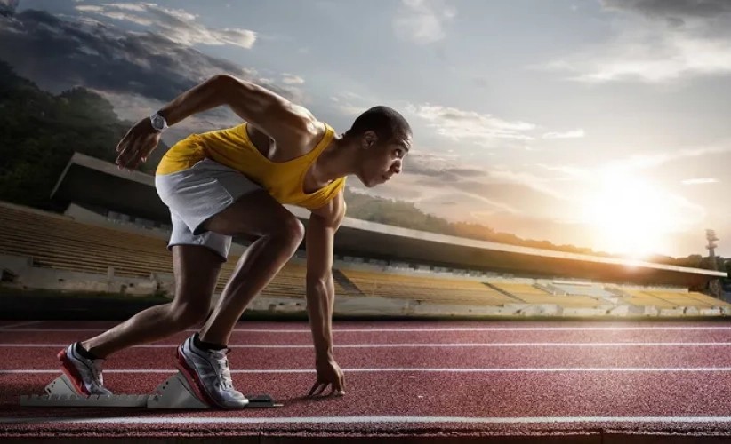 At sunrise, an athlete in a yellow tank top and white shorts channels focus akin to hypnosis therapy, preparing to sprint on the outdoor running track.