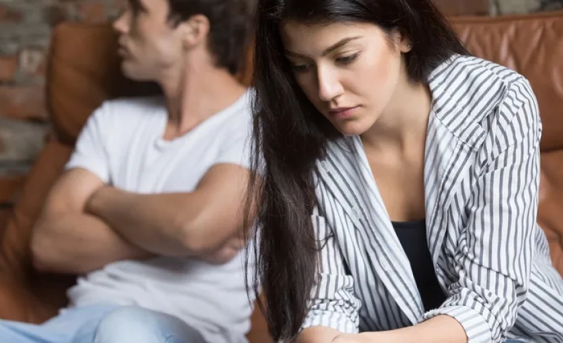 A woman in a striped blazer sits looking down as if lost in thought, while a man in a white shirt with his arms crossed looks away, both enveloped in a distant trance reminiscent of hypnosis therapy.