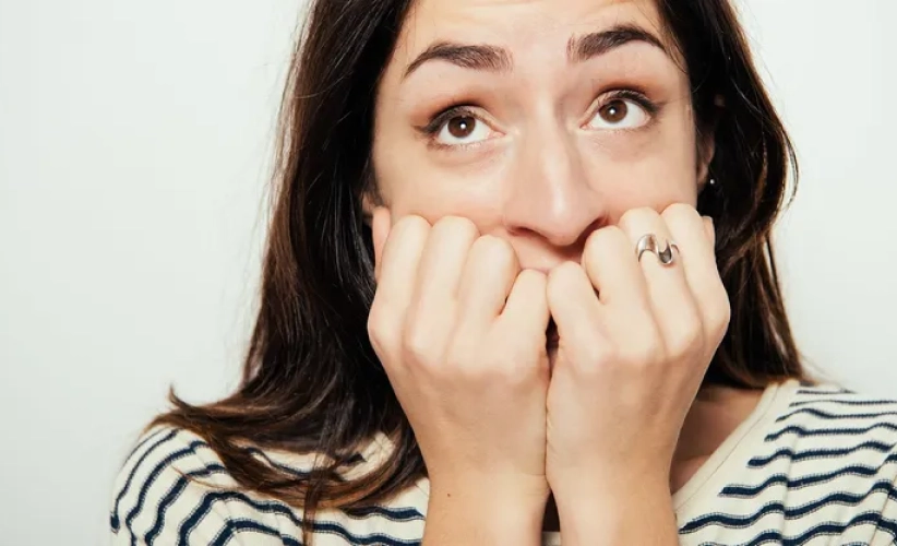 A woman with long dark hair bites her nails, looking upwards as if lost in thought. She is wearing a striped shirt and a ring on her finger, reminiscent of someone seeking solace or focus through hypnosis therapy.